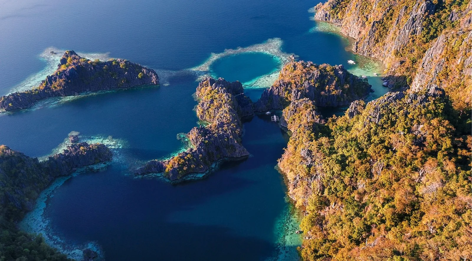 Aerial view of forested limestone islands, reef shallows and deep blue channels in northern Palawan