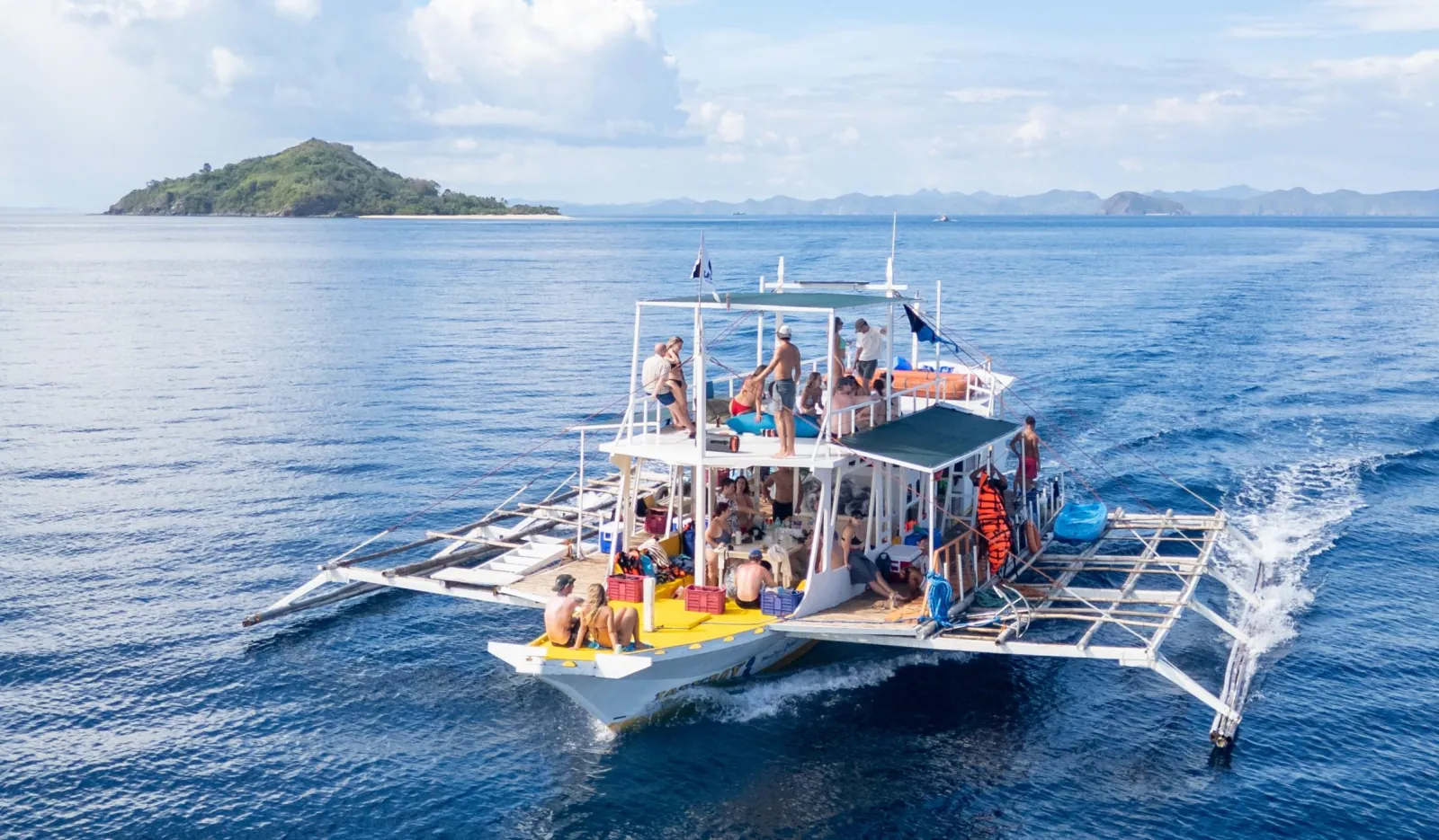 An outrigger expedition boat under way on open blue sea near a small island