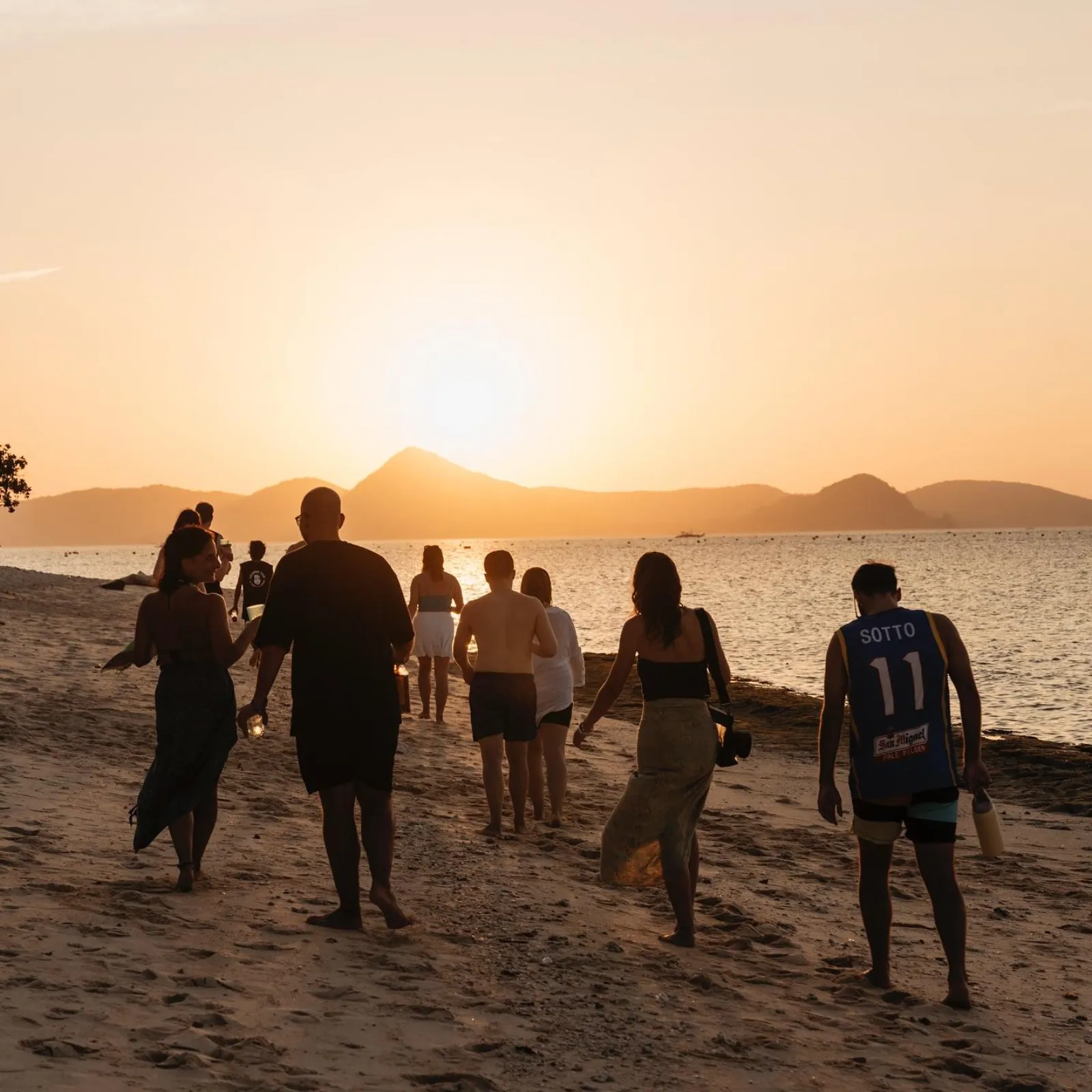 Travellers walking along the beach toward the setting sun