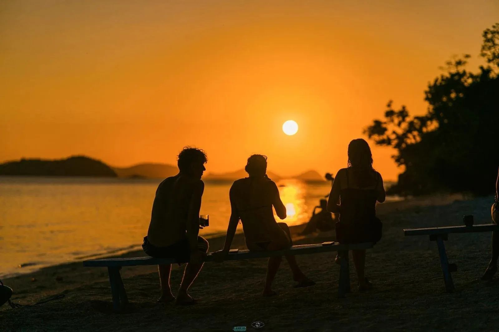Travellers silhouetted on a bench watching the sun set over the sea