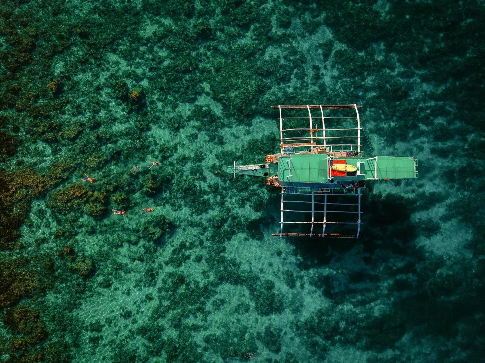 Aerial view of an outrigger boat over a shallow coral reef