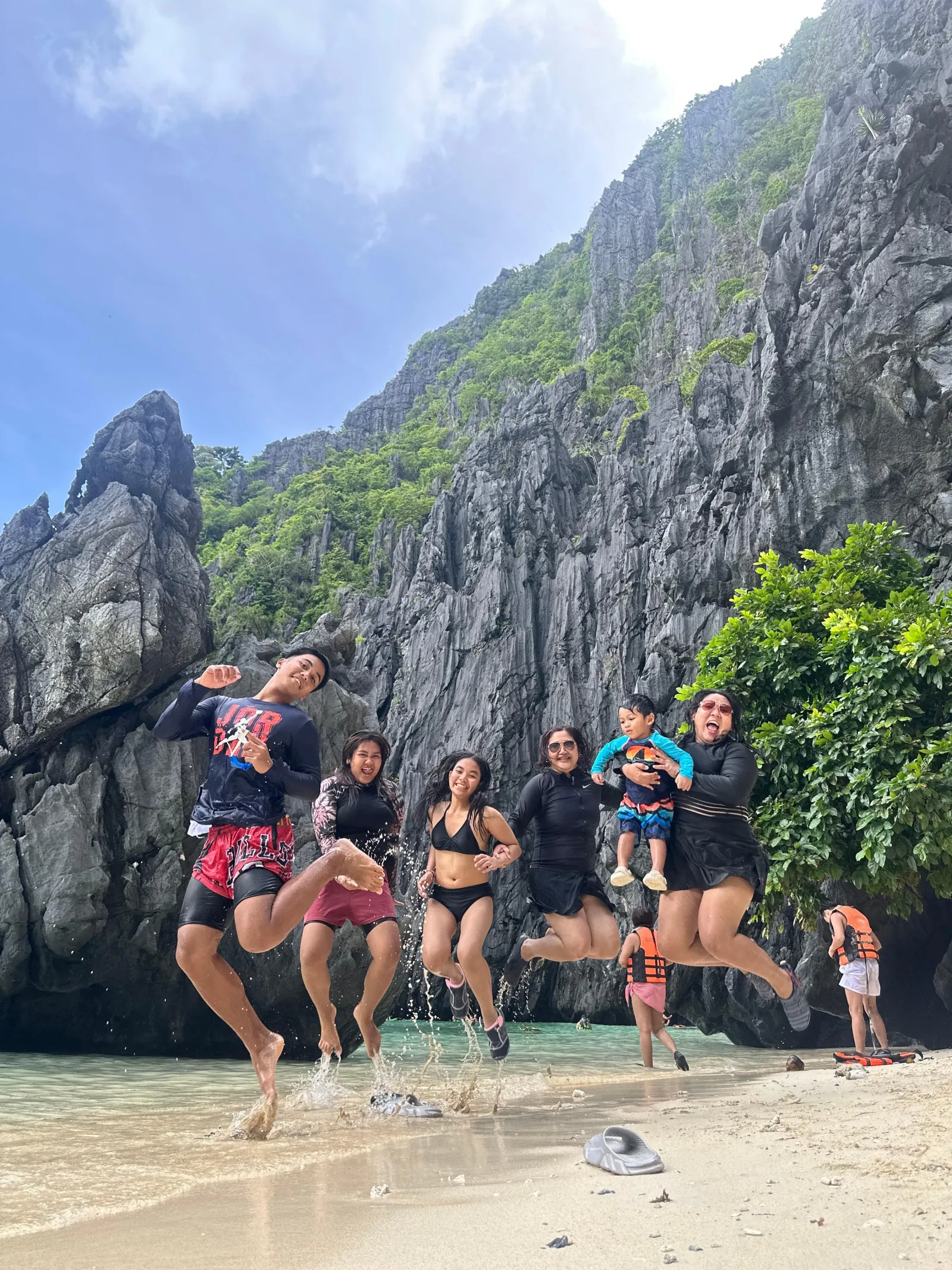 Travellers jumping for a photo on a beach in front of a limestone wall