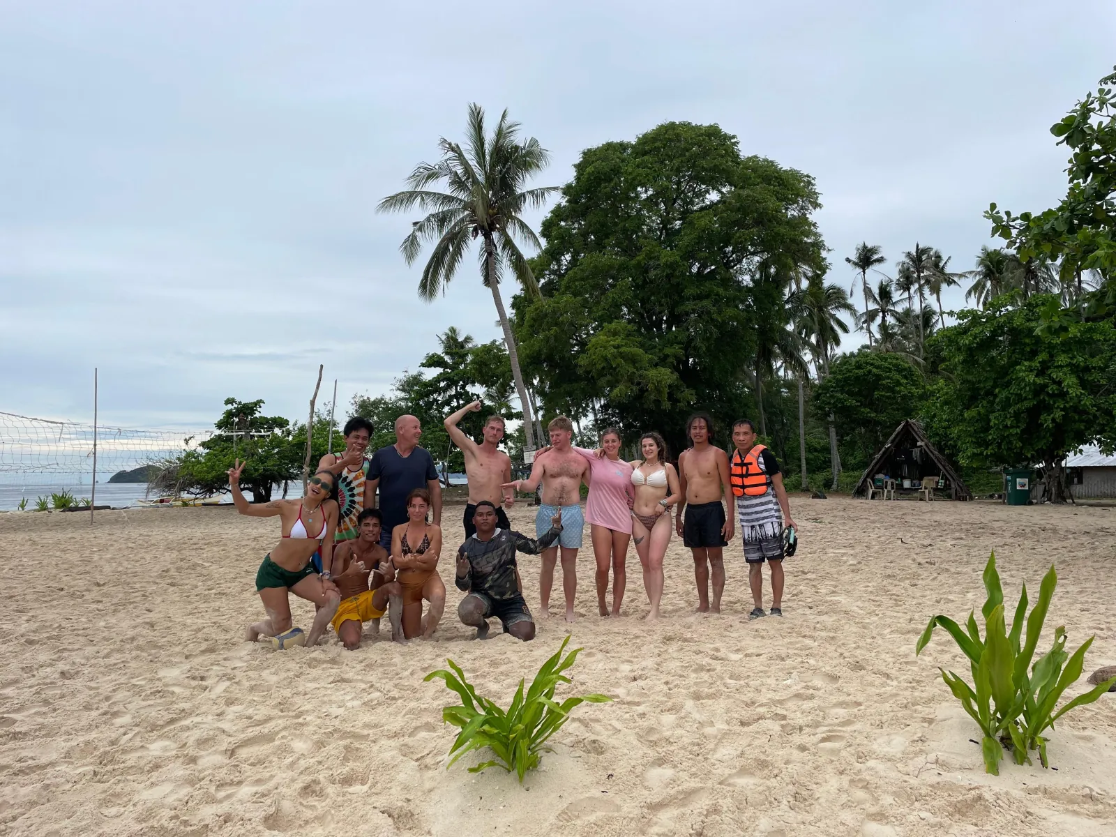 An expedition group posing on a white-sand beach lined with palms