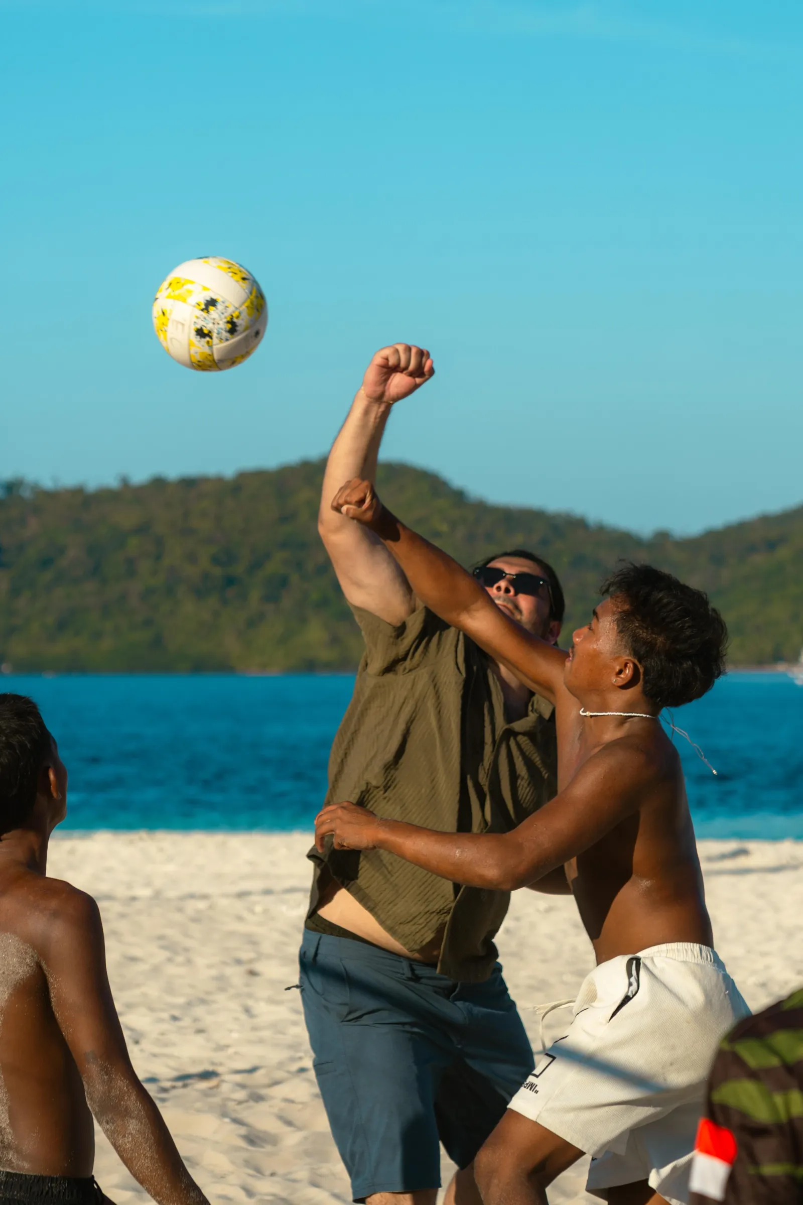Two men playing volleyball on a beach above blue water
