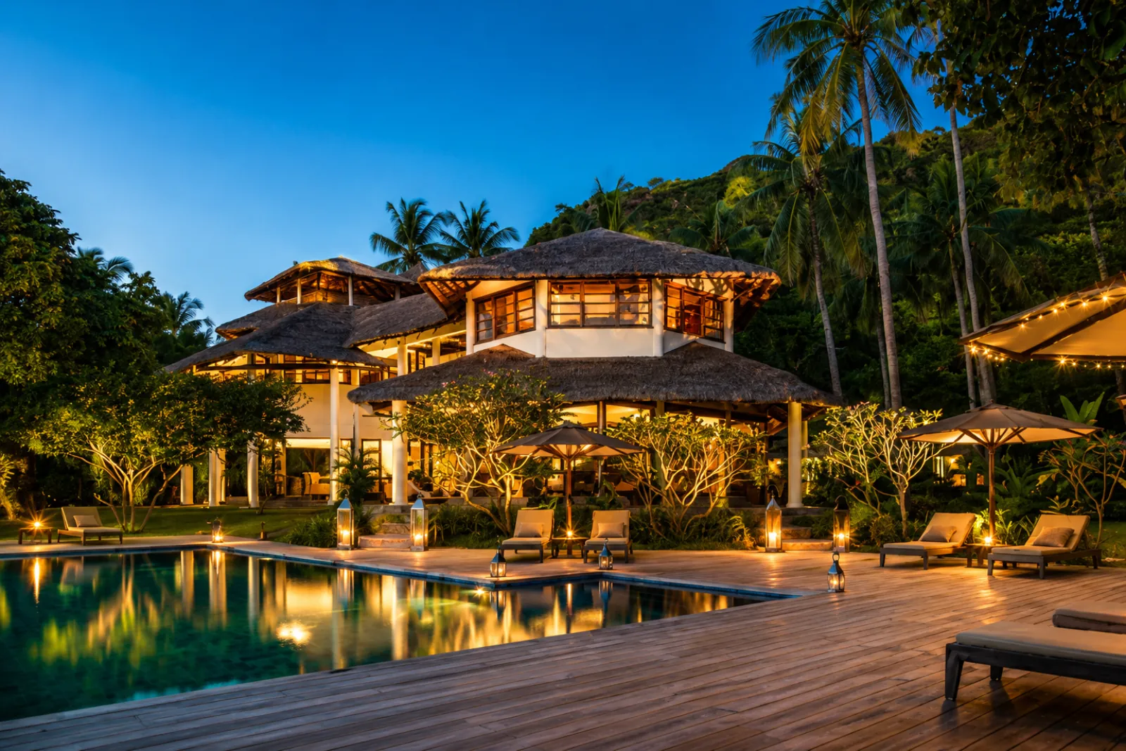 A lit resort villa and swimming pool among palm trees at dusk