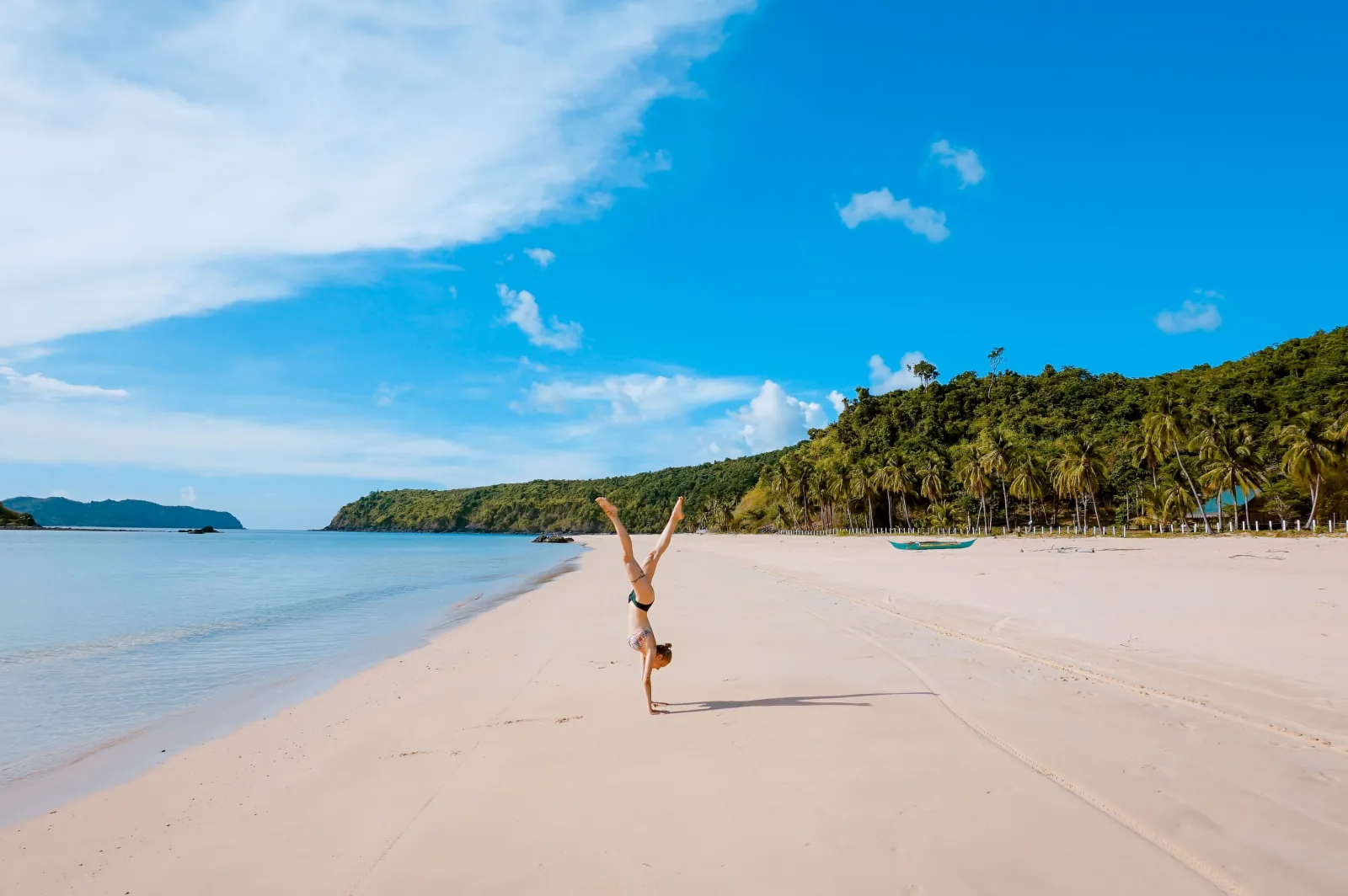 A person doing a handstand on a wide empty white-sand beach