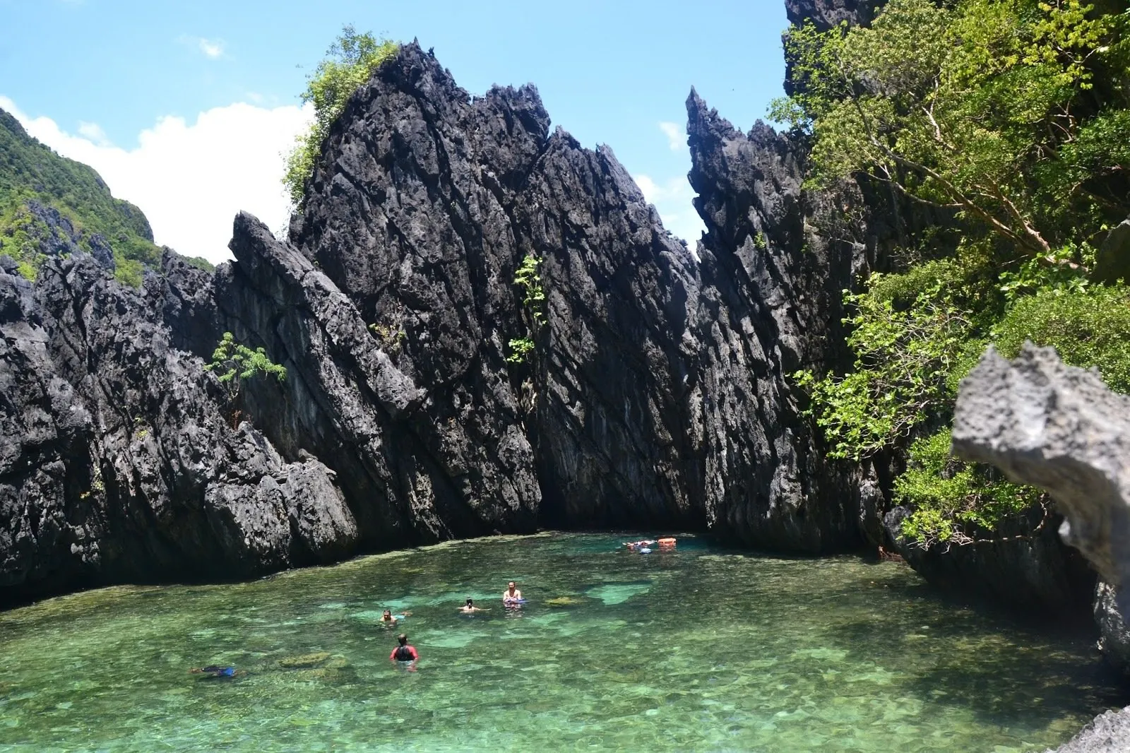 People swimming in a hidden beach cove enclosed by jagged limestone