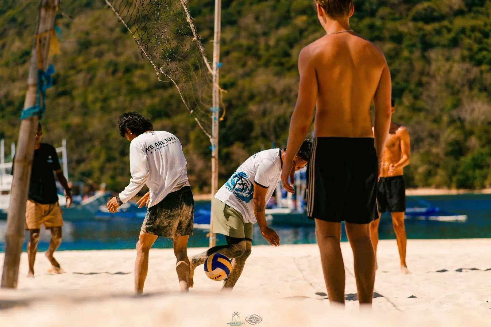 Guests and crew playing football barefoot on the beach at camp