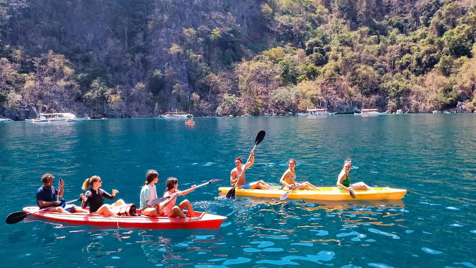 Kayakers paddling past limestone cliffs in Coron