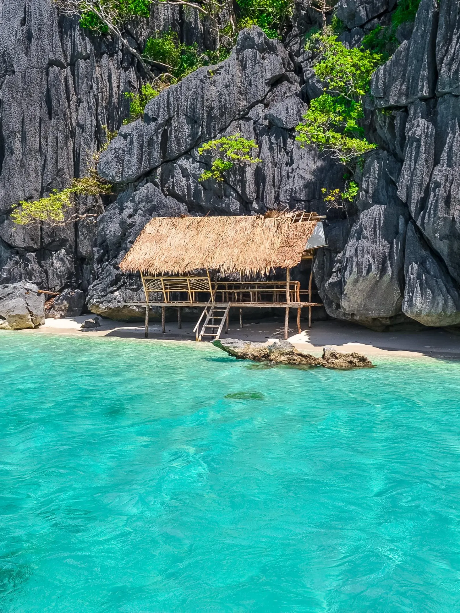 A thatched hut on stilts over turquoise water below limestone