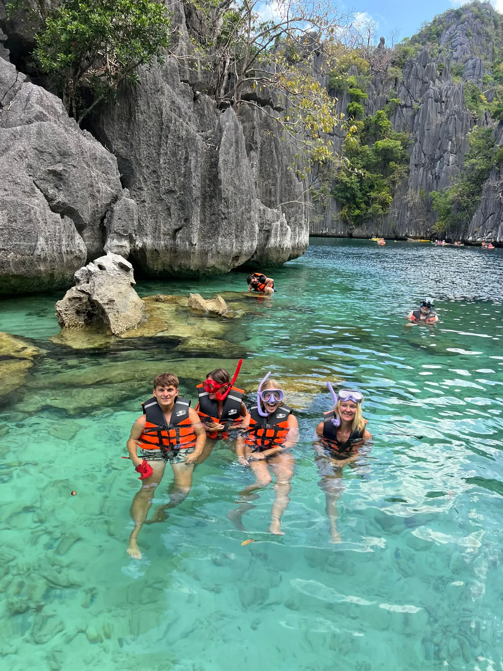 Swimmers in life jackets in a clear lagoon between limestone rocks
