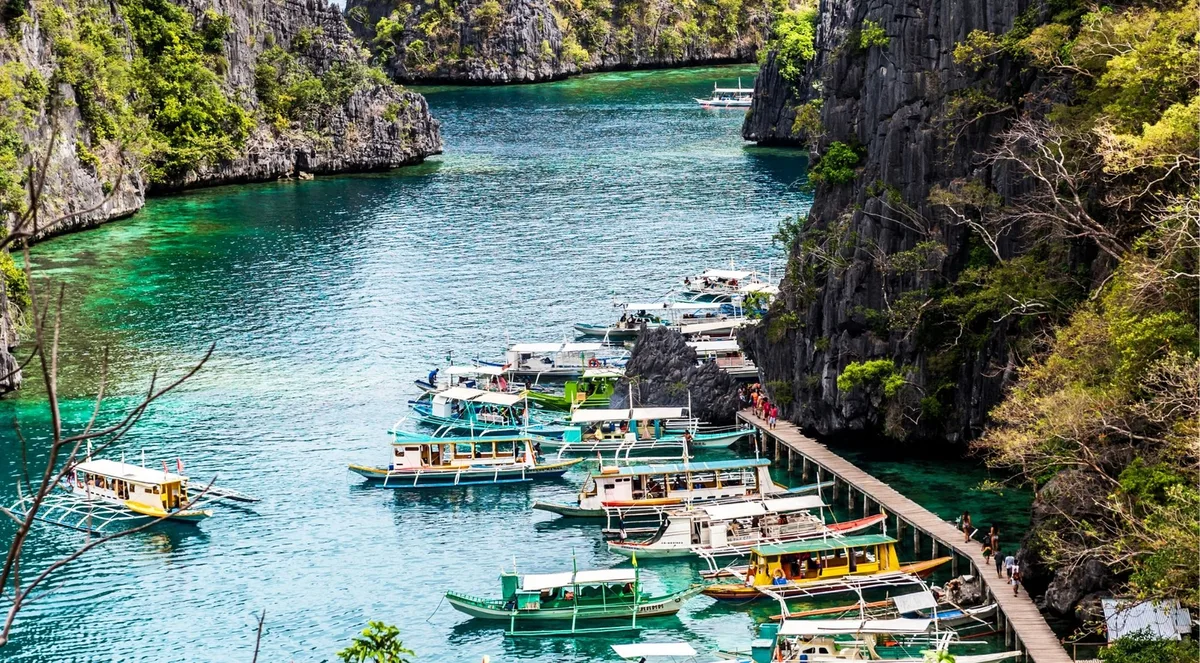 Outrigger boats moored along a wooden boardwalk in a narrow limestone inlet